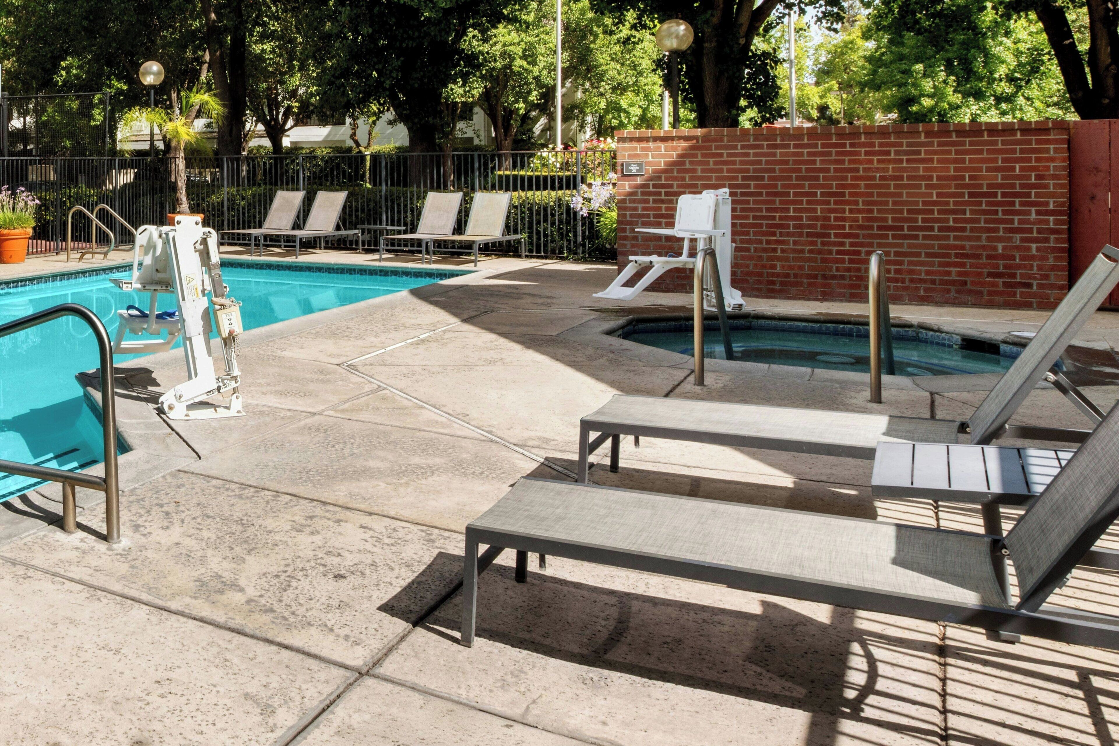A pool area with lounge chairs, a pool ladder, and a brick wall.