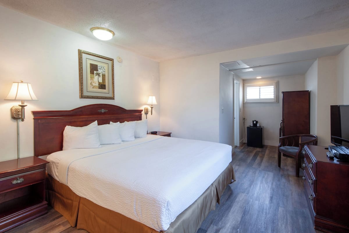 Habitación de hotel con una cama grande, lámparas de noche, un cabecero de madera, un escritorio con una silla, un aparador, un televisor y un cuadro en la pared.
