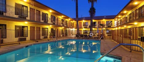 A hotel with a swimming pool, multiple balconies, and palm trees.