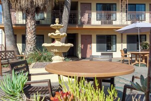 Un patio al aire libre con una mesa y sillas de madera redonda, una fuente de piedra y una palmera.