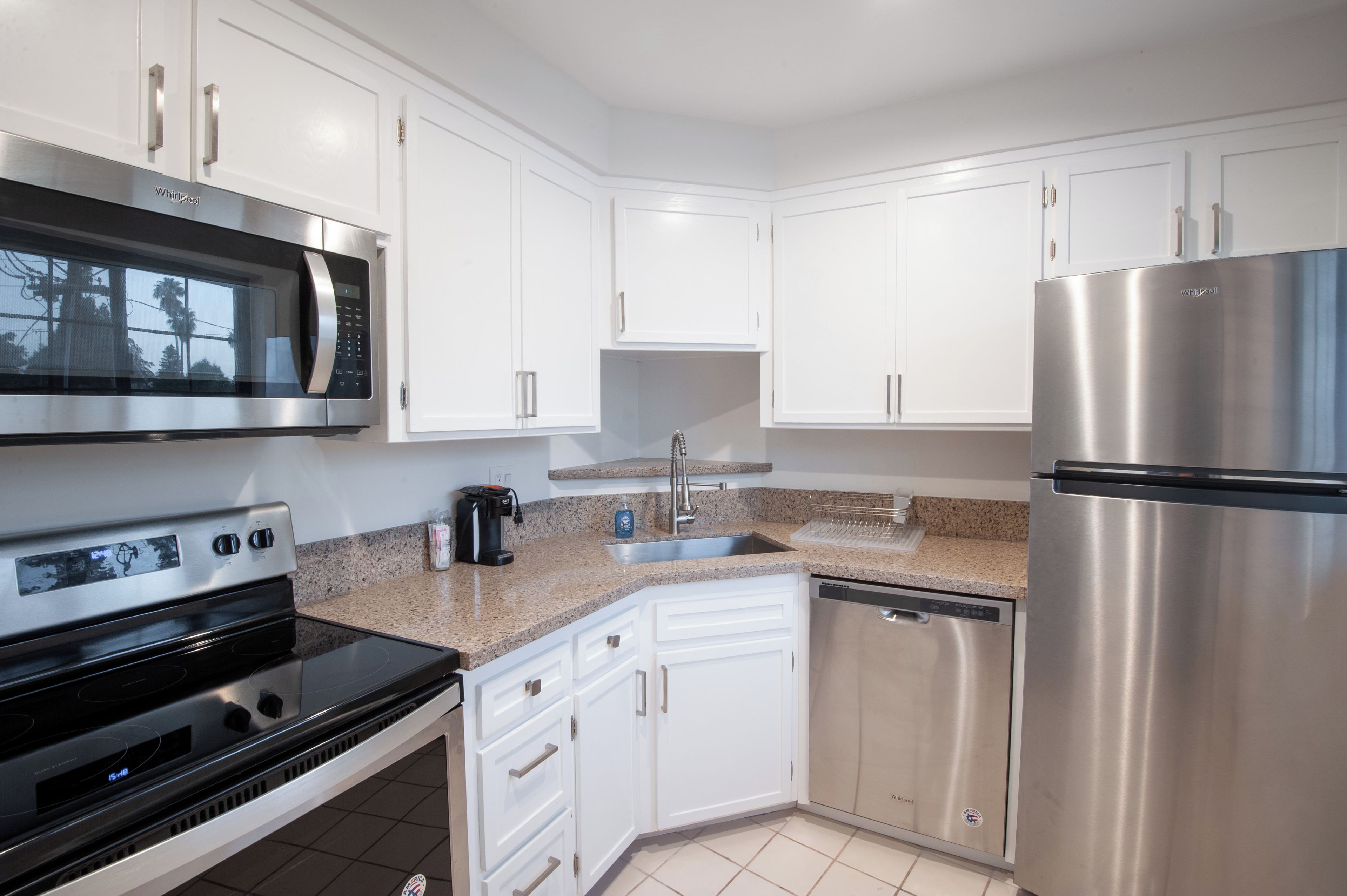 Una cocina moderna con armarios blancos, electrodomésticos de acero inoxidable, incluyendo un microondas, horno y refrigerador, y una encimera de granito.