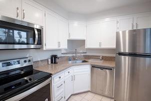 Una cocina moderna con armarios blancos, electrodomésticos de acero inoxidable, incluyendo un microondas, horno y refrigerador, y una encimera de granito.