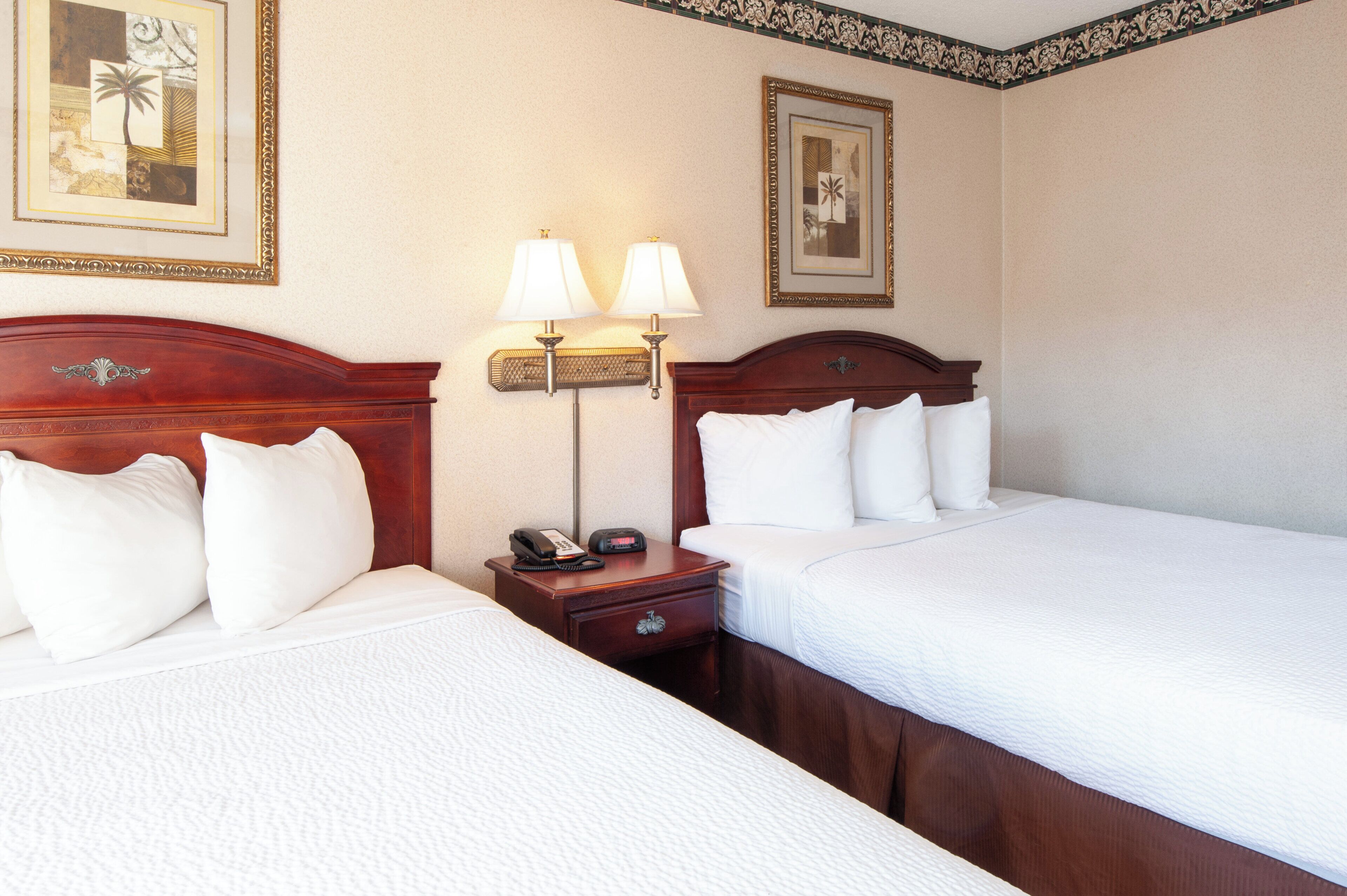 Une chambre d’hôtel avec deux lits, une table de chevet avec une lampe et des tableaux encadrés au mur.