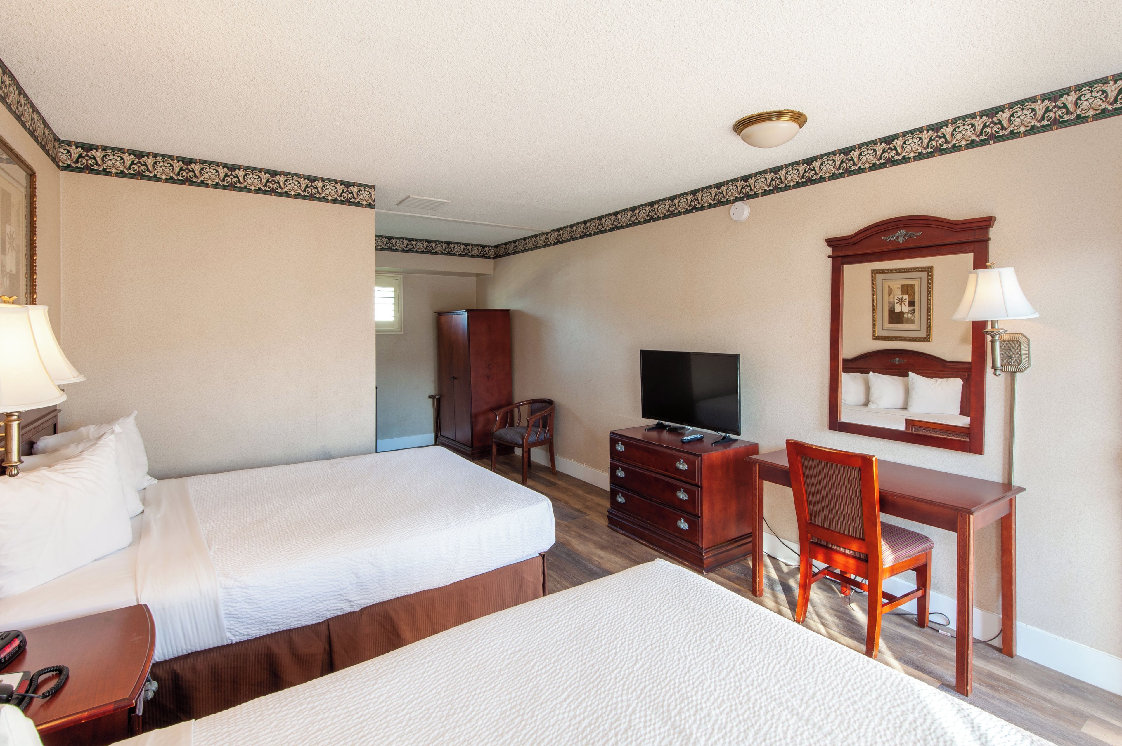 Habitación de hotel con dos camas, un escritorio con una silla, un televisor y un aparador.