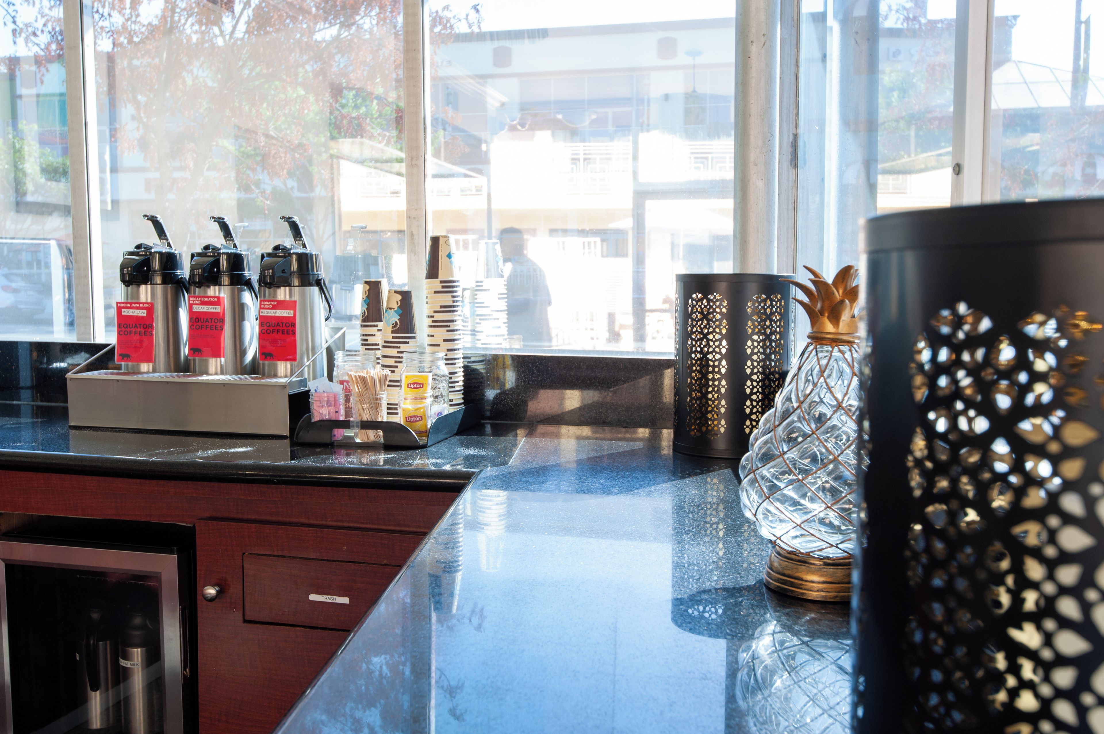 Un espace dédié au café, équipé de machines à expresso et d’une cafetière, ainsi qu’un vase en verre décoratif et un récipient à motifs.