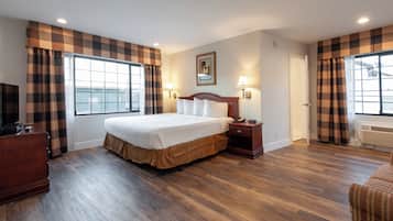 Una habitación de hotel con una cama grande, dos lámparas de noche, un aparador de madera y una ventana con cortinas a cuadros.