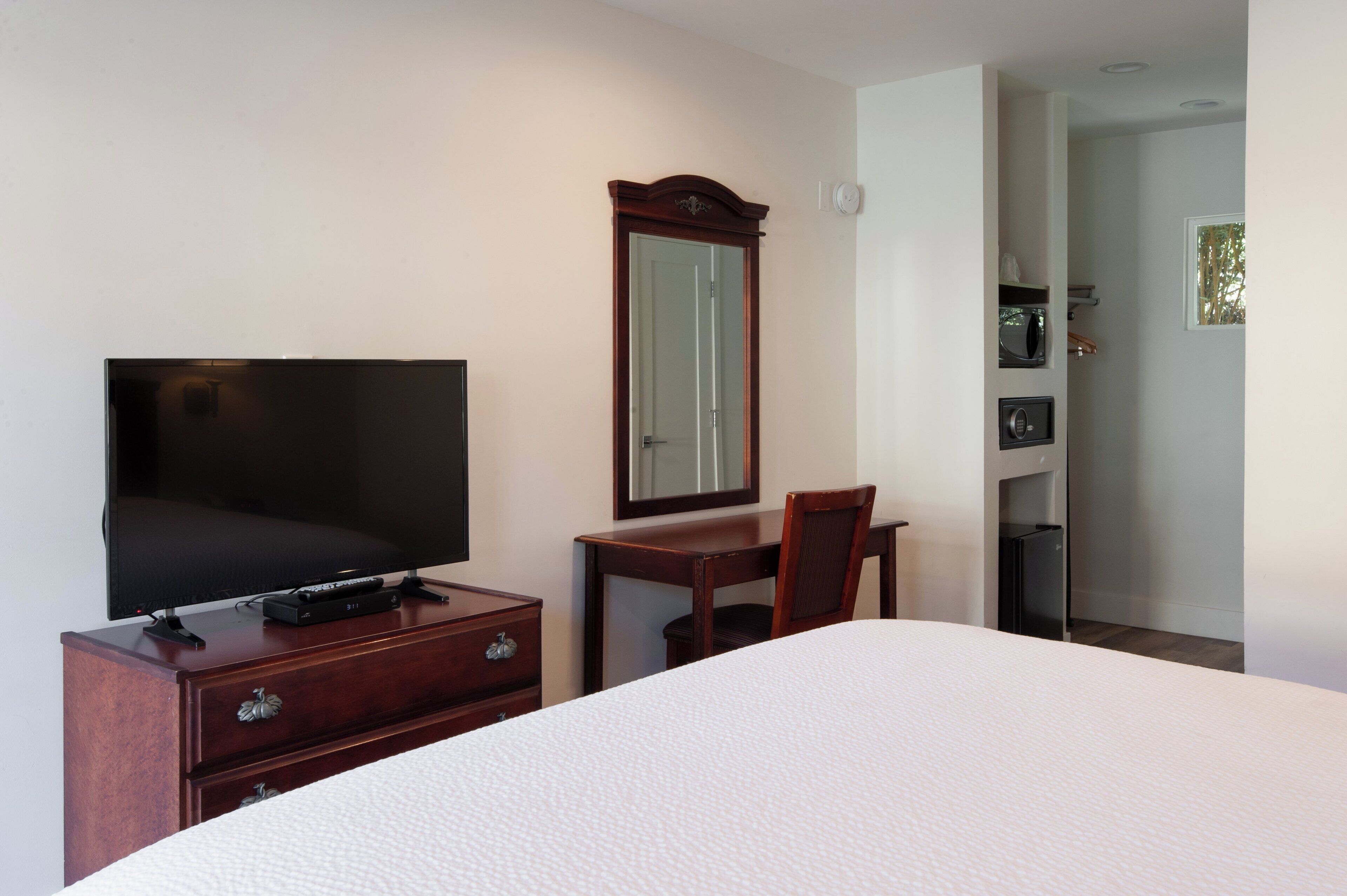 A hotel room with a bed, a TV on a wooden dresser, a mirror, and a door leading to a bathroom.