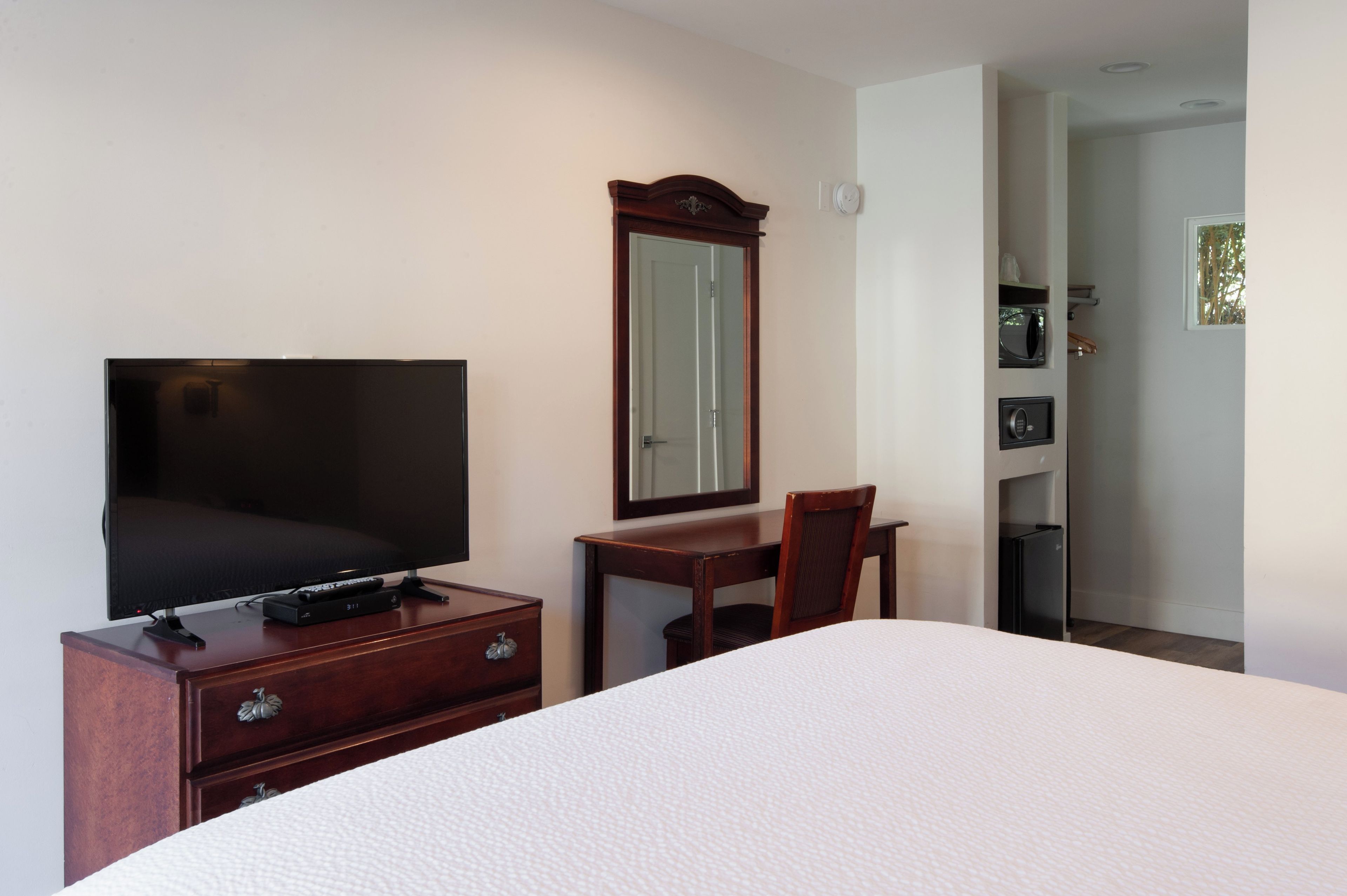 Habitación de hotel con cama, televisor sobre una cómoda de madera, un espejo y una puerta que da al baño.