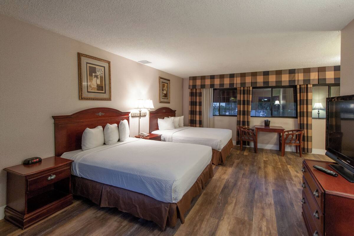 Una habitación de hotel con dos camas, un escritorio, un televisor y una ventana con cortinas.