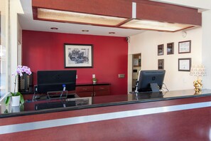 A reception desk with two HP computers, a framed picture on the wall, and a potted plant. - Studio City Court Yard Hotel (Studio City)