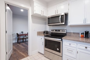 A modern kitchen with white cabinets, a microwave, an oven, and a dining area with a table and chairs. - Studio City Court Yard Hotel (Studio City)
