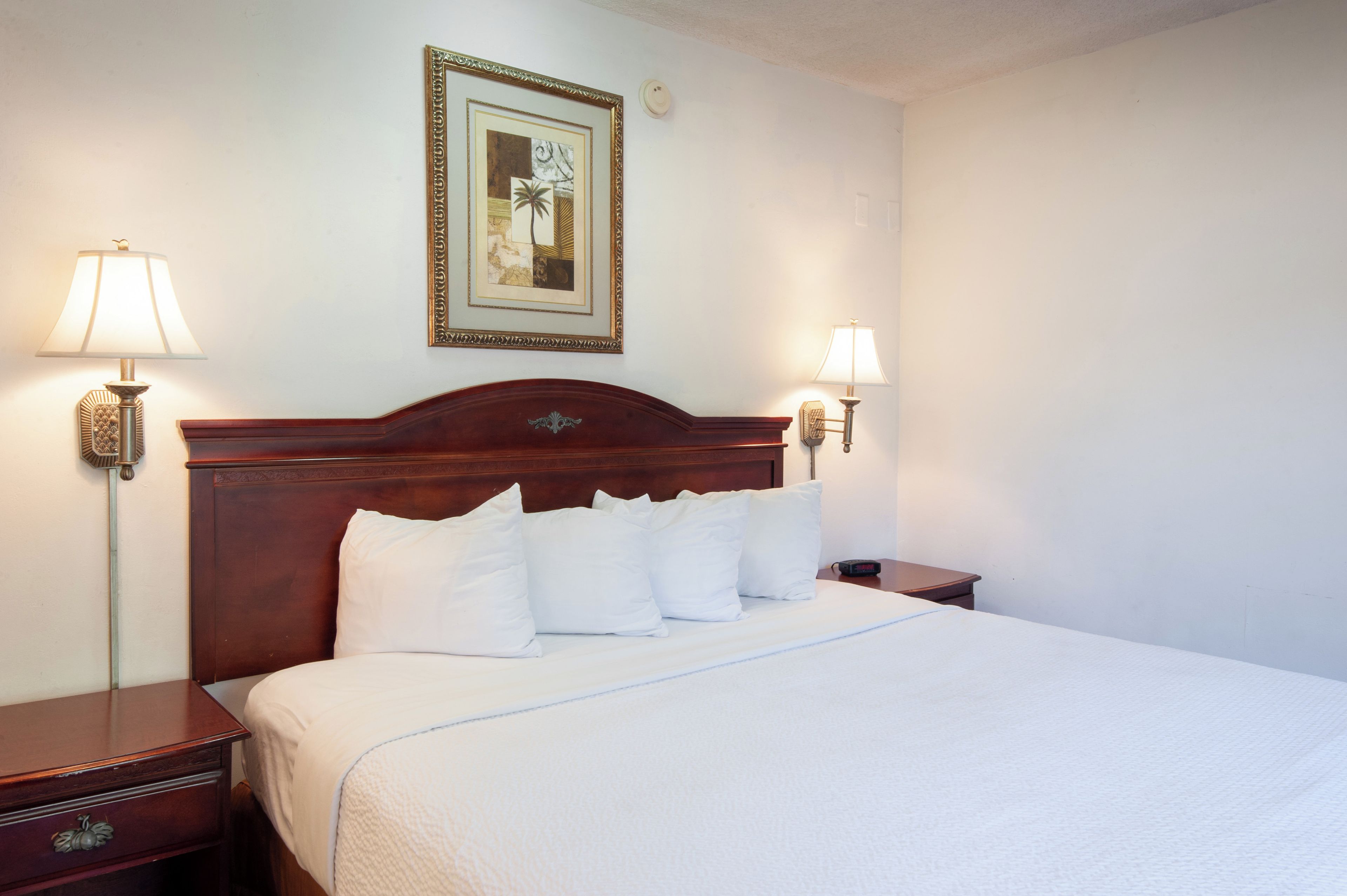 Una cama bien hecha con sábanas y almohadas blancas, un cabecero de madera y dos lámparas de noche a cada lado.