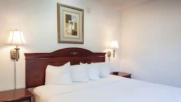 A neatly made bed with white linens and pillows, a wooden headboard, and two bedside lamps on either side.