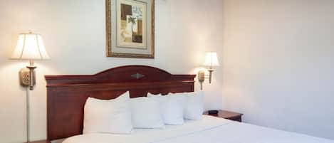 A neatly made bed with white linens and pillows, a wooden headboard, and two bedside lamps on either side.