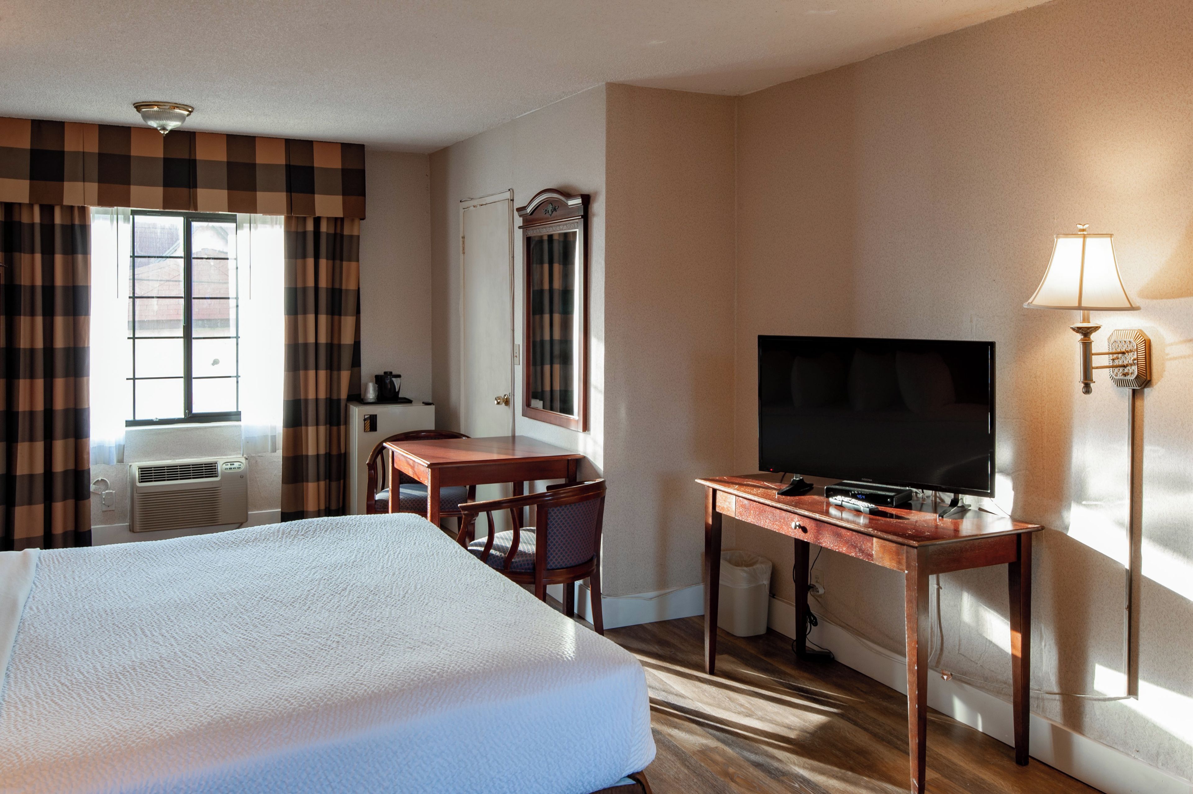 A hotel room with a bed, a desk, a television, and a window with curtains.