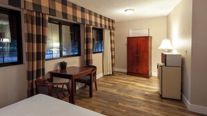 A hotel room with a checkered curtain, a wooden desk with a chair, a bed, a wardrobe, and a refrigerator. - Studio City Court Yard Hotel (Studio City)