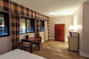 A hotel room with a checkered curtain, a wooden desk with a chair, a bed, a wardrobe, and a refrigerator. - Studio City Court Yard Hotel (Studio City)