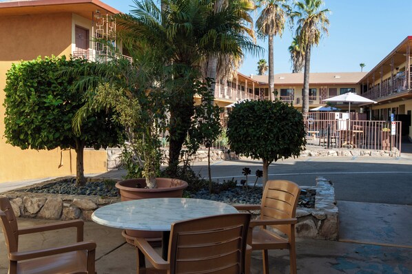 An outdoor seating area with a round table and chairs, surrounded by potted plants and a palm tree. - Studio City Court Yard Hotel (Studio City)