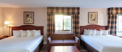 Habitación de hotel con dos camas, un sofá, una mesa de centro de madera y una lámpara.