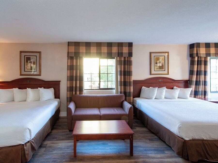 A hotel room with two beds, a sofa, a wooden coffee table, and a lamp.