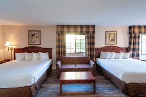 Habitación de hotel con dos camas, un sofá, una mesa de centro de madera y una lámpara.