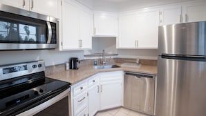 A modern kitchen with white cabinets, stainless steel appliances including a microwave, oven, and refrigerator, and a granite countertop. - Studio City Court Yard Hotel (Studio City)