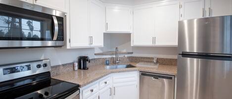 Una cocina moderna con armarios blancos, electrodomésticos de acero inoxidable, incluyendo un microondas, horno y refrigerador, y una encimera de granito.