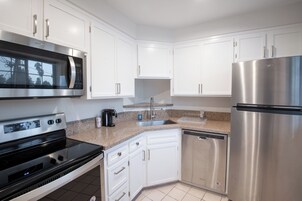 Una cocina moderna con armarios blancos, electrodomésticos de acero inoxidable, incluyendo un microondas, horno y refrigerador, y una encimera de granito.