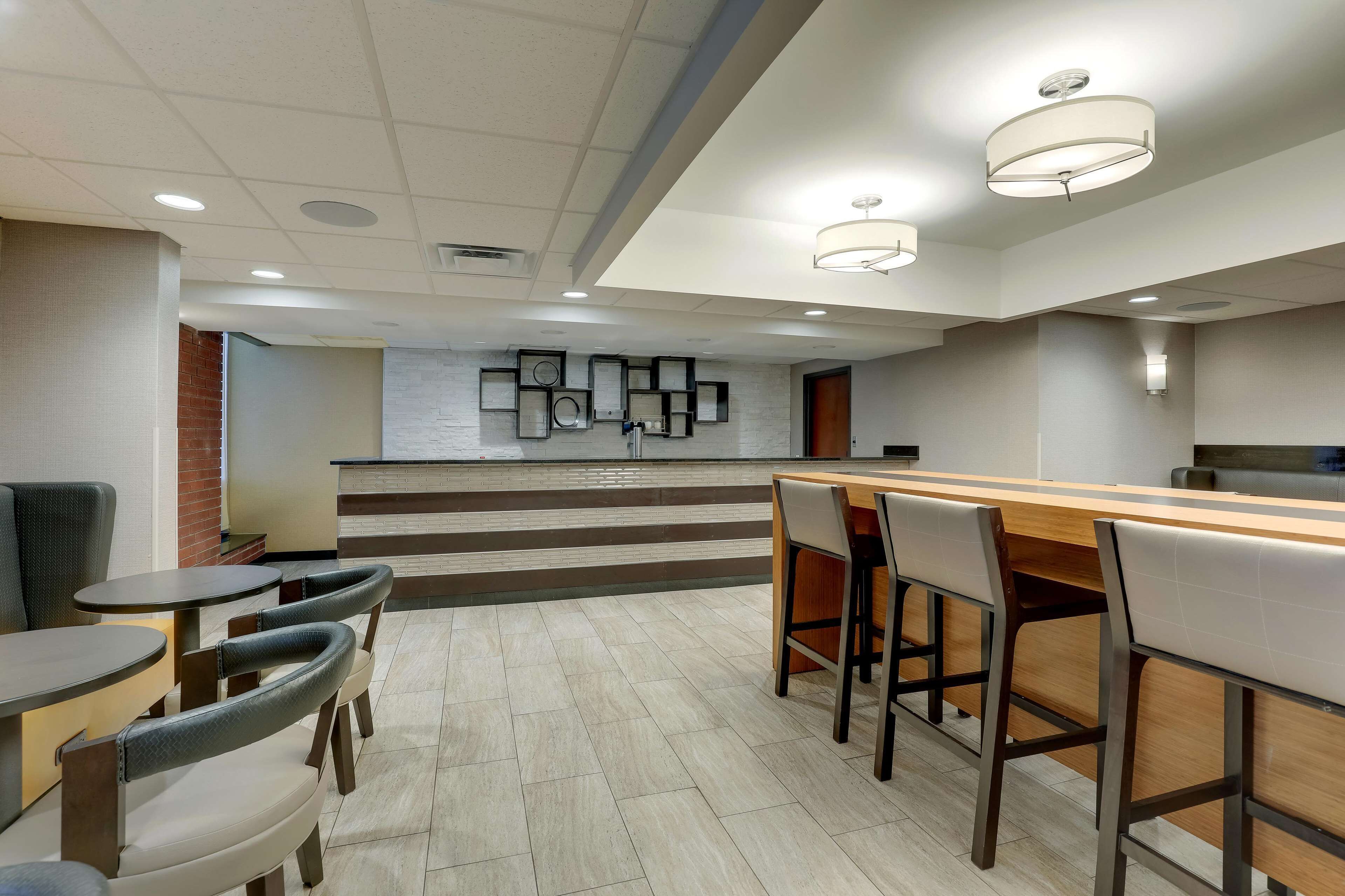 A modern hotel lobby with a reception desk, seating area, and a staircase leading to the upper floor.