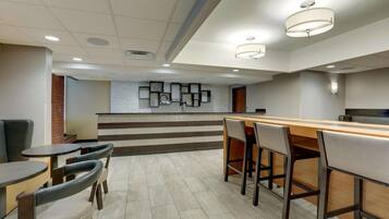 A modern hotel lobby with a reception desk, seating area, and a staircase leading to the upper floor.