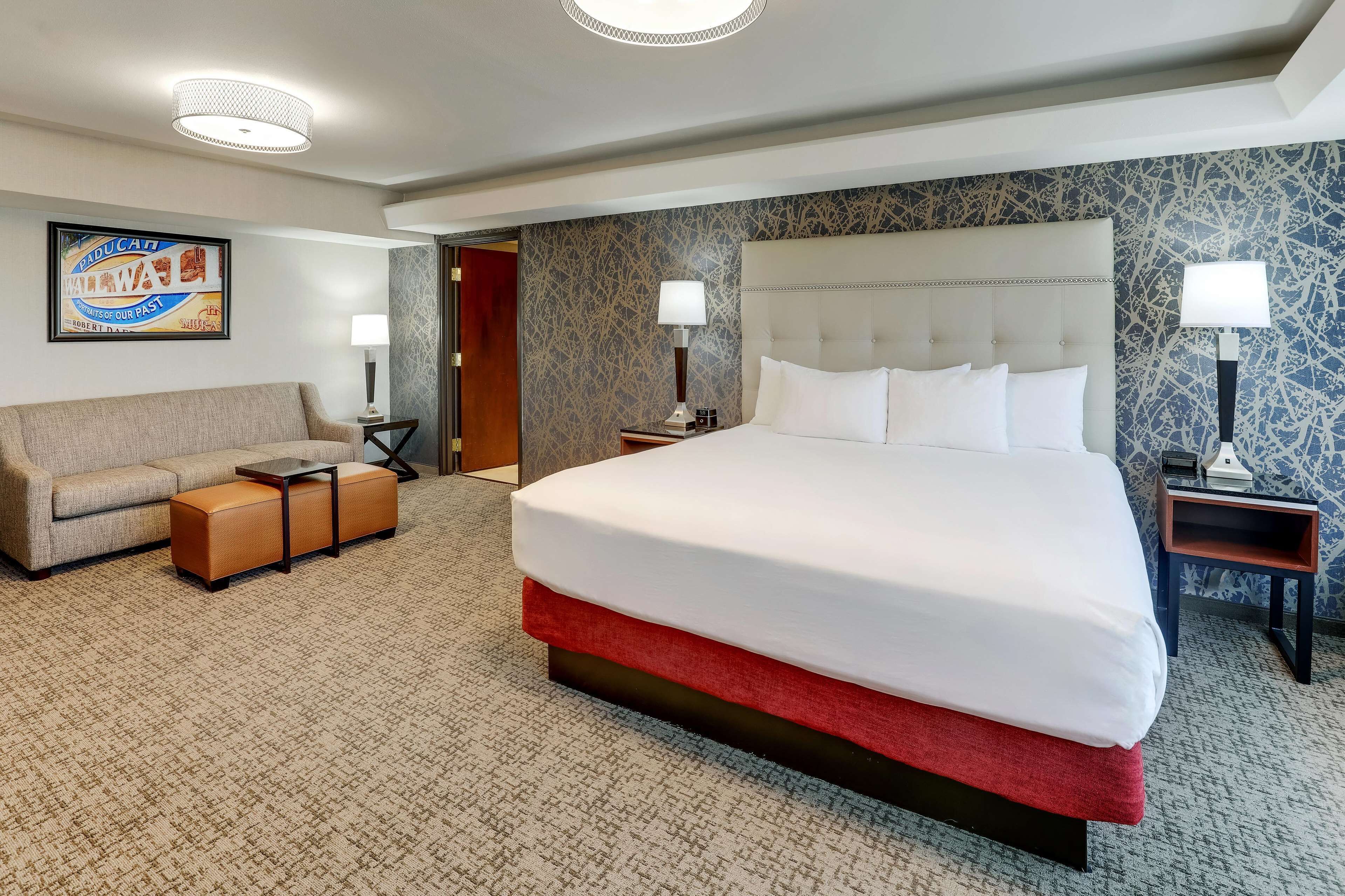 A hotel room with a large bed, a sofa, a small table, and two nightstands with lamps.