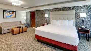 A hotel room with a large bed, a sofa, a small table, and two nightstands with lamps.