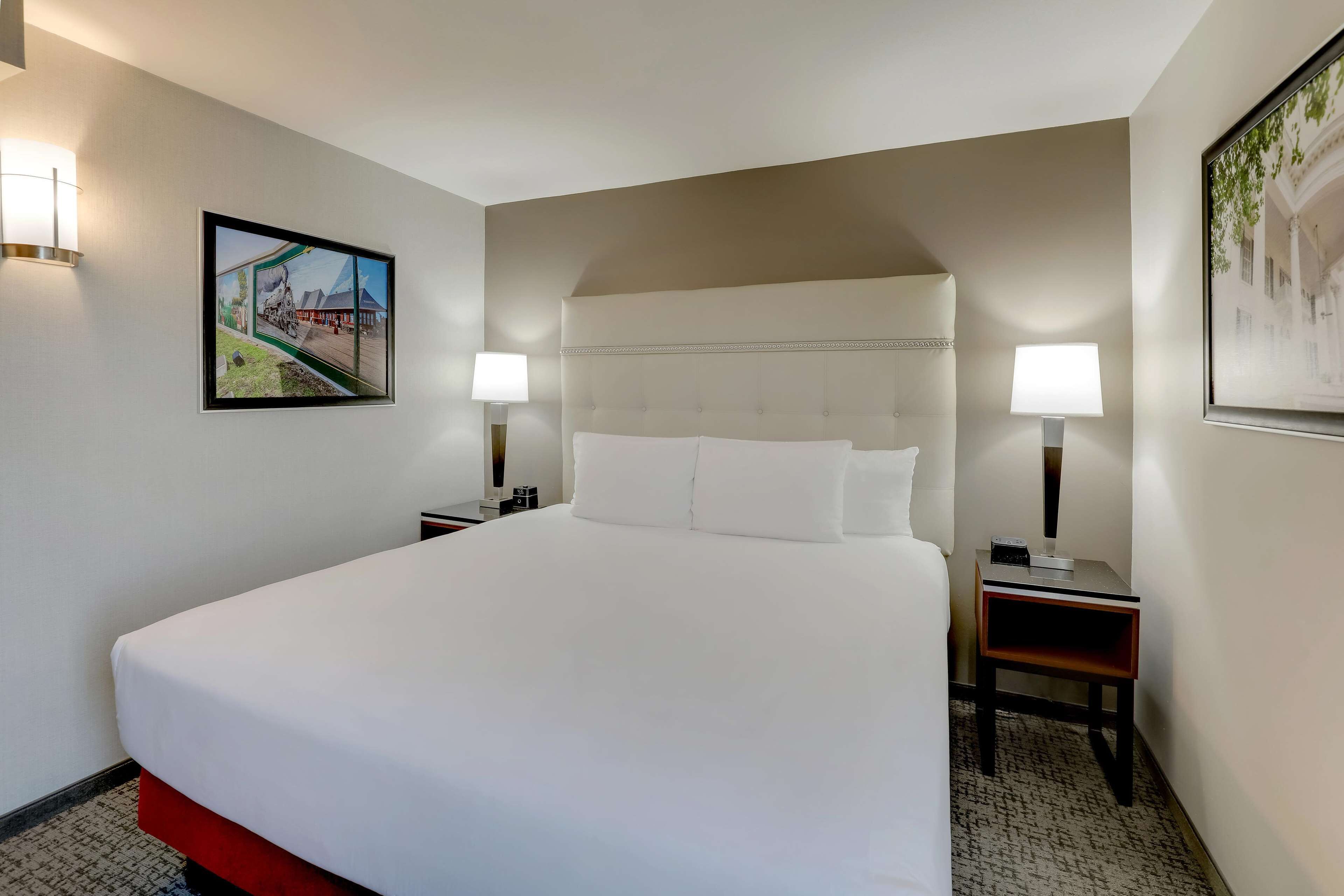 A hotel room with a large bed, two bedside tables, a wall-mounted lamp, and a framed picture on the wall.
