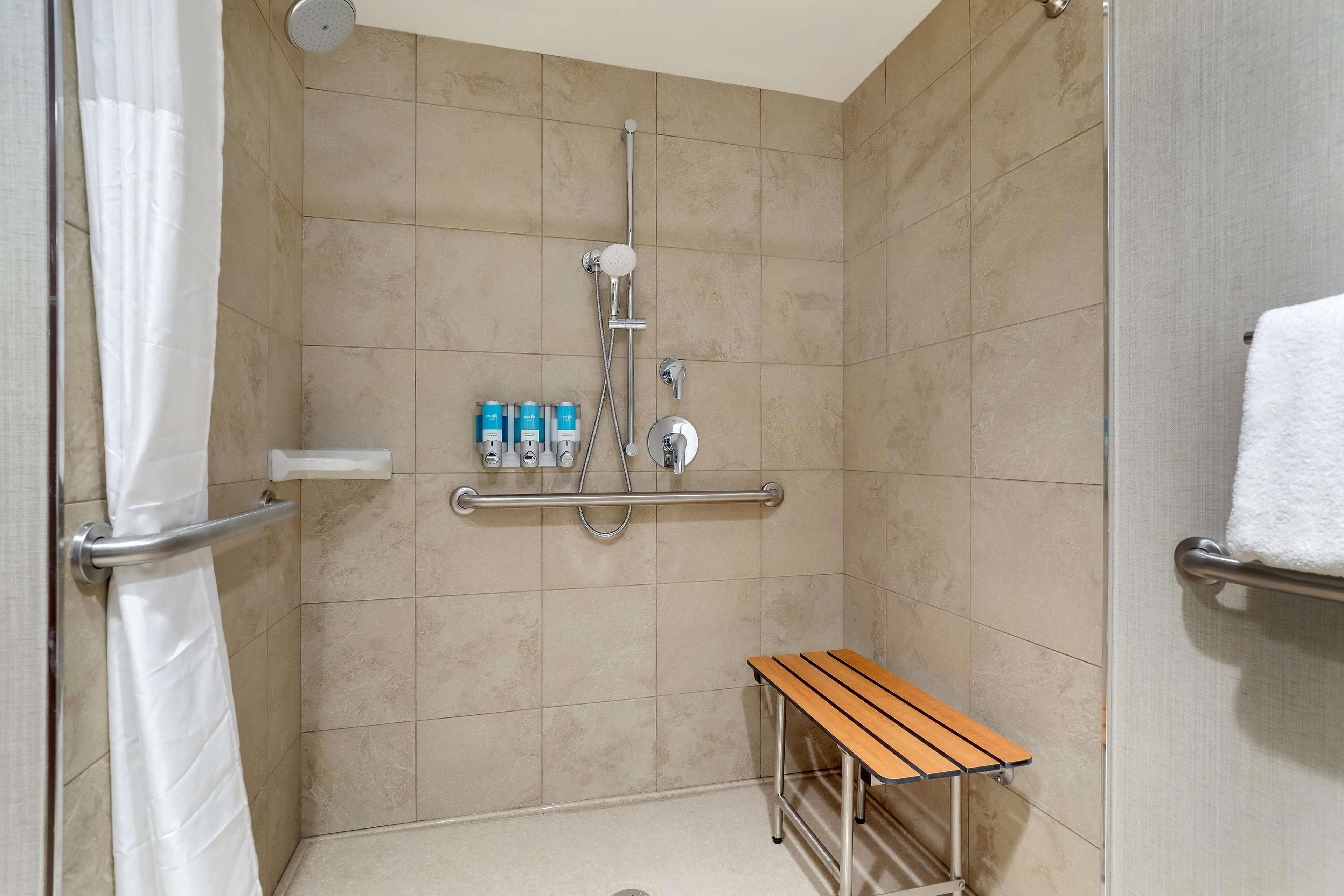 Un espace douche avec des carreaux de couleur beige, une douchette à main, un robinet mural et un banc en bois.