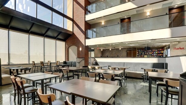 A modern indoor dining area with multiple tables and chairs, a glass railing, and a view of a bookstore in the background. - Drury Inn Paducah (Paducah)