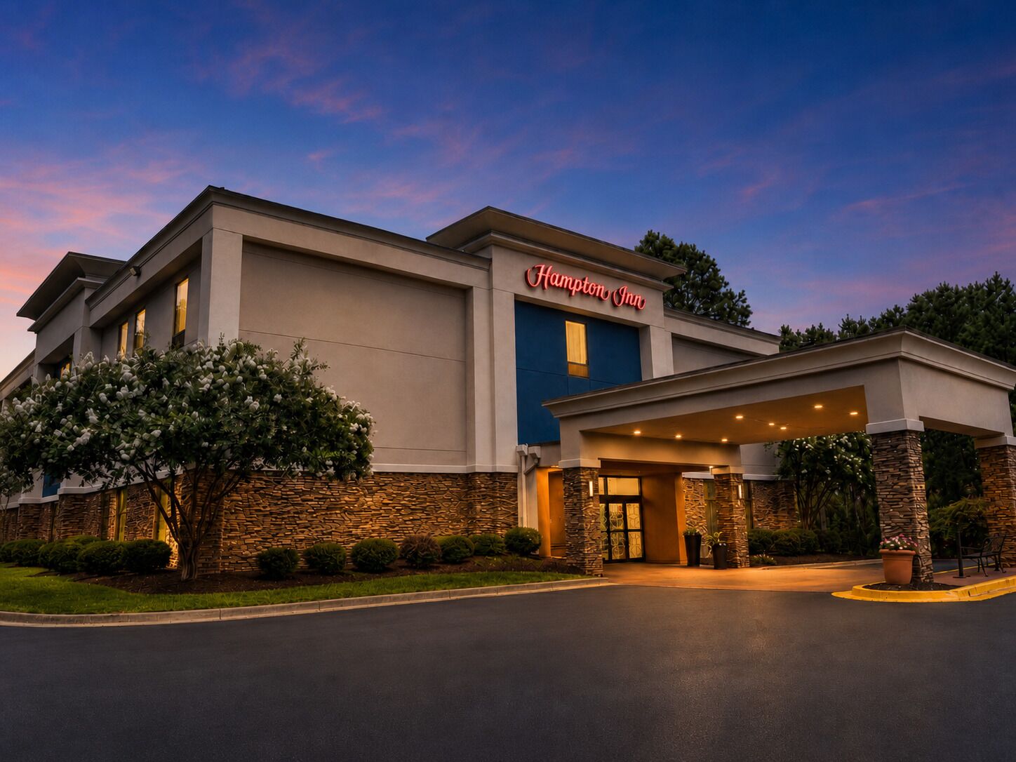 A Hampton Inn hotel with a modern facade, stone accents, and a welcoming entrance.