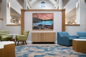 Un hall moderno con un cuadro grande de un paisaje, dos sillones, una consola de madera y una alfombra estampada.