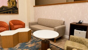 Habitación de hotel con sofá, dos sillones, una mesa de centro, alfombra estampada, un cuadro de un edificio, un teléfono e impresora.