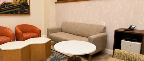 A hotel room with a sofa, two armchairs, a coffee table, a patterned rug, a painting of a building, a telephone, and a printer.