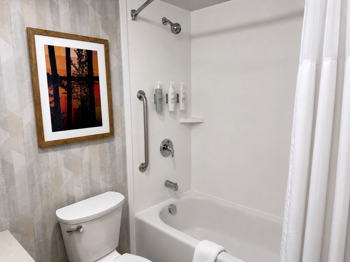 A bathroom with a toilet, a bathtub, and a shower. There is a framed picture on the wall.