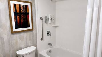 A bathroom with a toilet, a bathtub, and a shower. There is a framed picture on the wall.