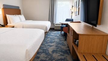 A hotel room with two beds, a desk, a television, and a window with curtains.