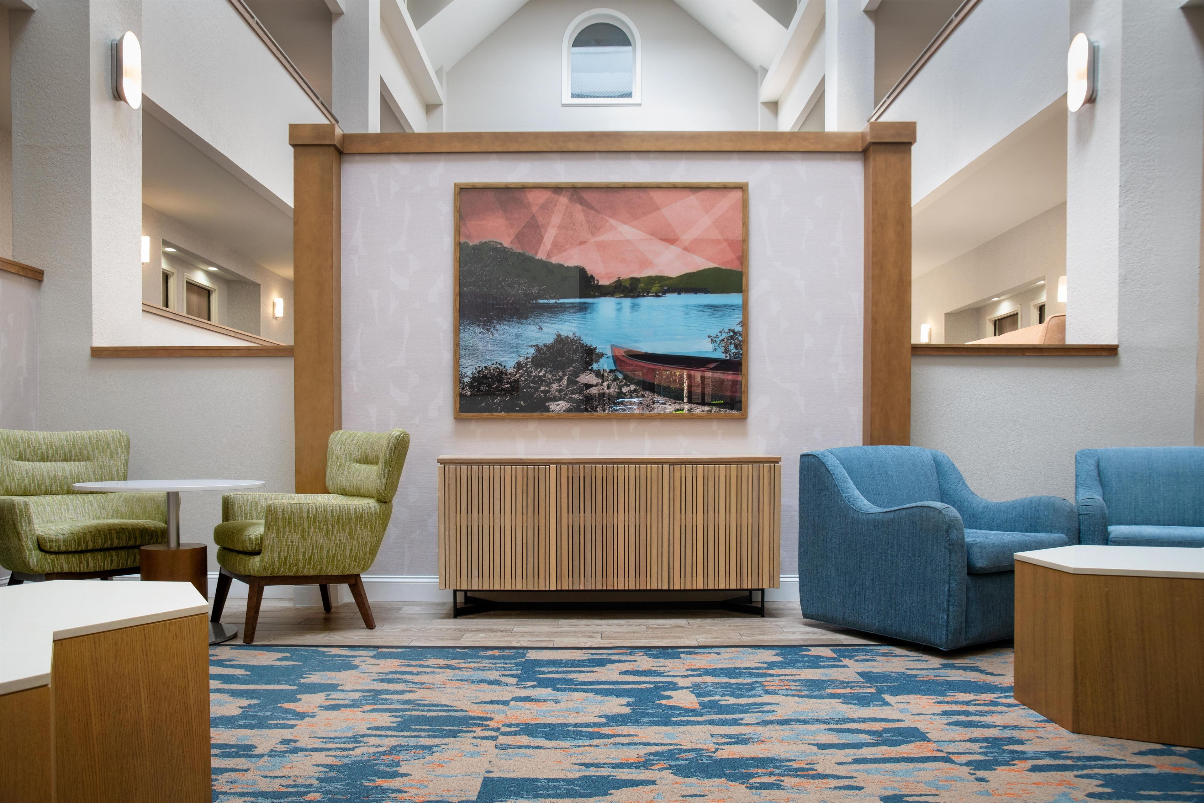 A modern lobby with a large painting of a landscape, two armchairs, a wooden console table, and a patterned rug.