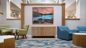 A modern lobby with a large painting of a landscape, two armchairs, a wooden console table, and a patterned rug.