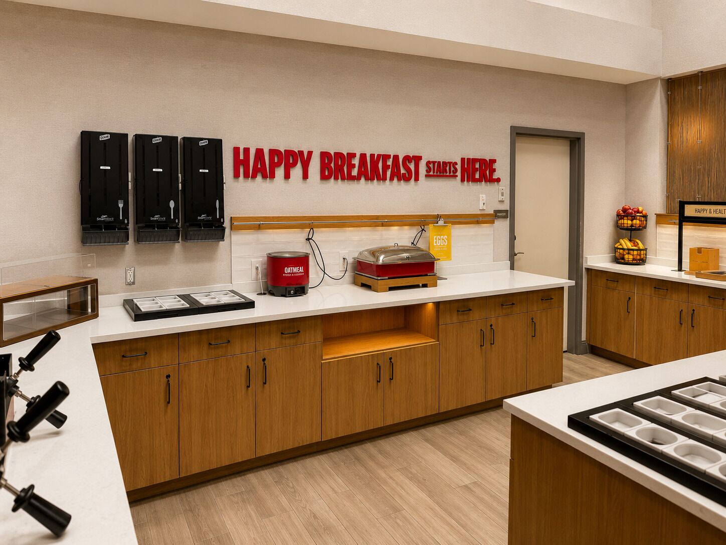 A breakfast area with a sign that reads 'HAPPY BREAKFAST STARTS HERE.' There are black cabinets with utensils, a red oatmeal dispenser, and a fruit basket on the counter.