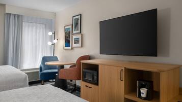 A hotel room with a bed, a desk with a microwave, a coffee machine, a TV, and a chair.