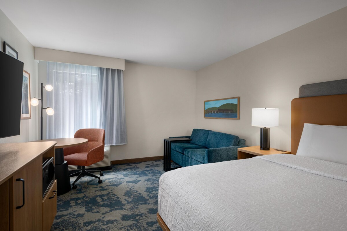 Een hotelkamer met een bed, een bureau met stoel, een bank, een lamp en een schilderij aan de muur.
