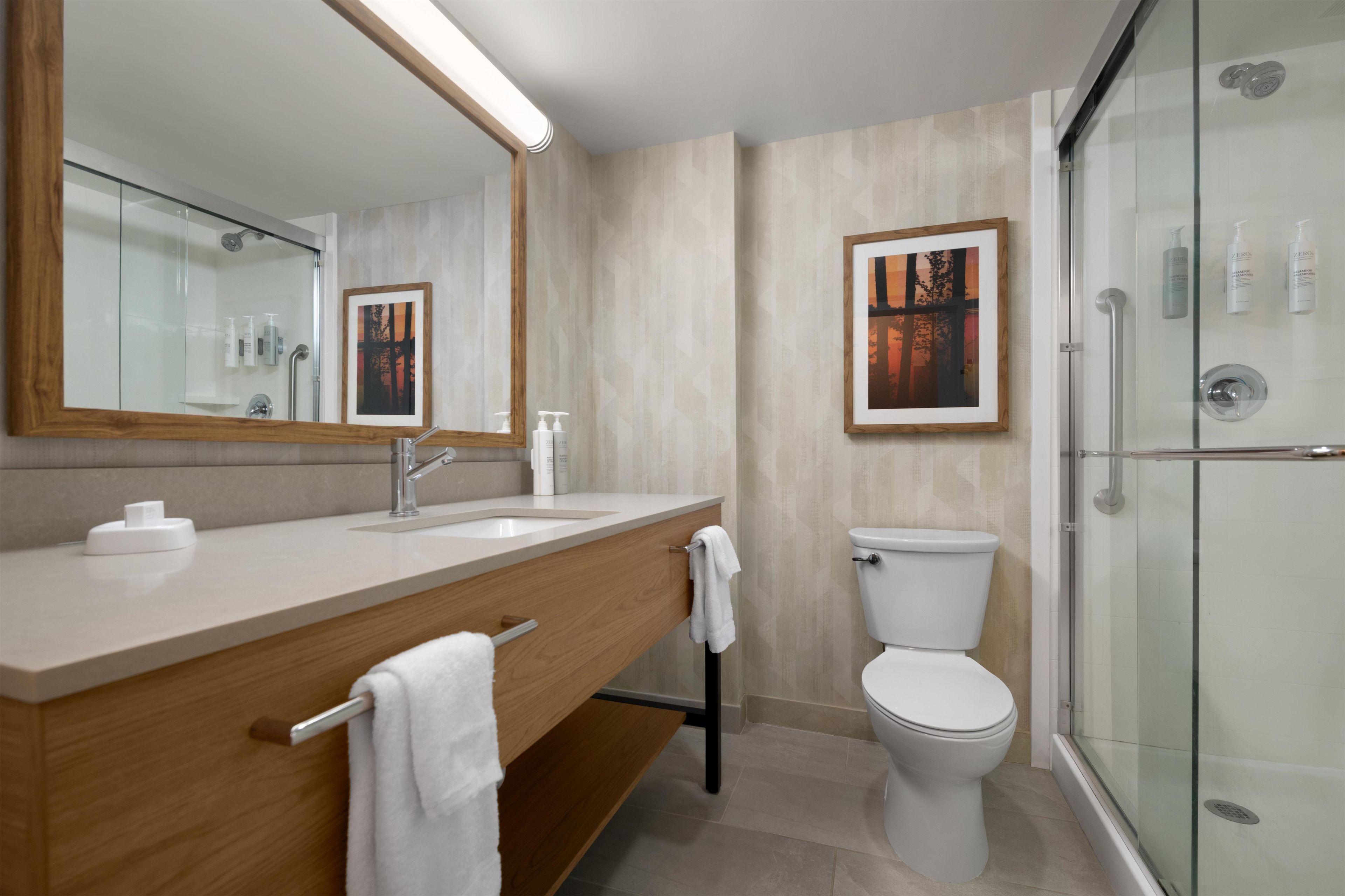 Un baño moderno con un espejo grande, un tocador de madera, un inodoro y una cabina de ducha con paredes de vidrio.