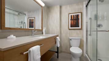 Un baño moderno con un espejo grande, un tocador de madera, un inodoro y una cabina de ducha con paredes de vidrio.