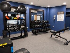 A gym with exercise equipment, including kettlebells, dumbbells, and a bench.